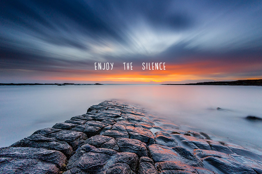 Tranquil long exposure photo of the sea washing over rocks with 'Enjoy the Silence' quote
